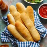 overhead view of breadsticks in a basket with gingham napkin with salad and marinara on the side.