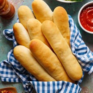 Overhead view of sourdough discard breadsticks in a basket with marinara sauce and salad.