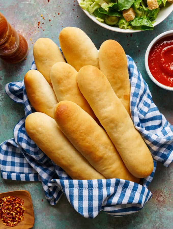 Overhead view of sourdough discard breadsticks in a basket with marinara sauce and salad.