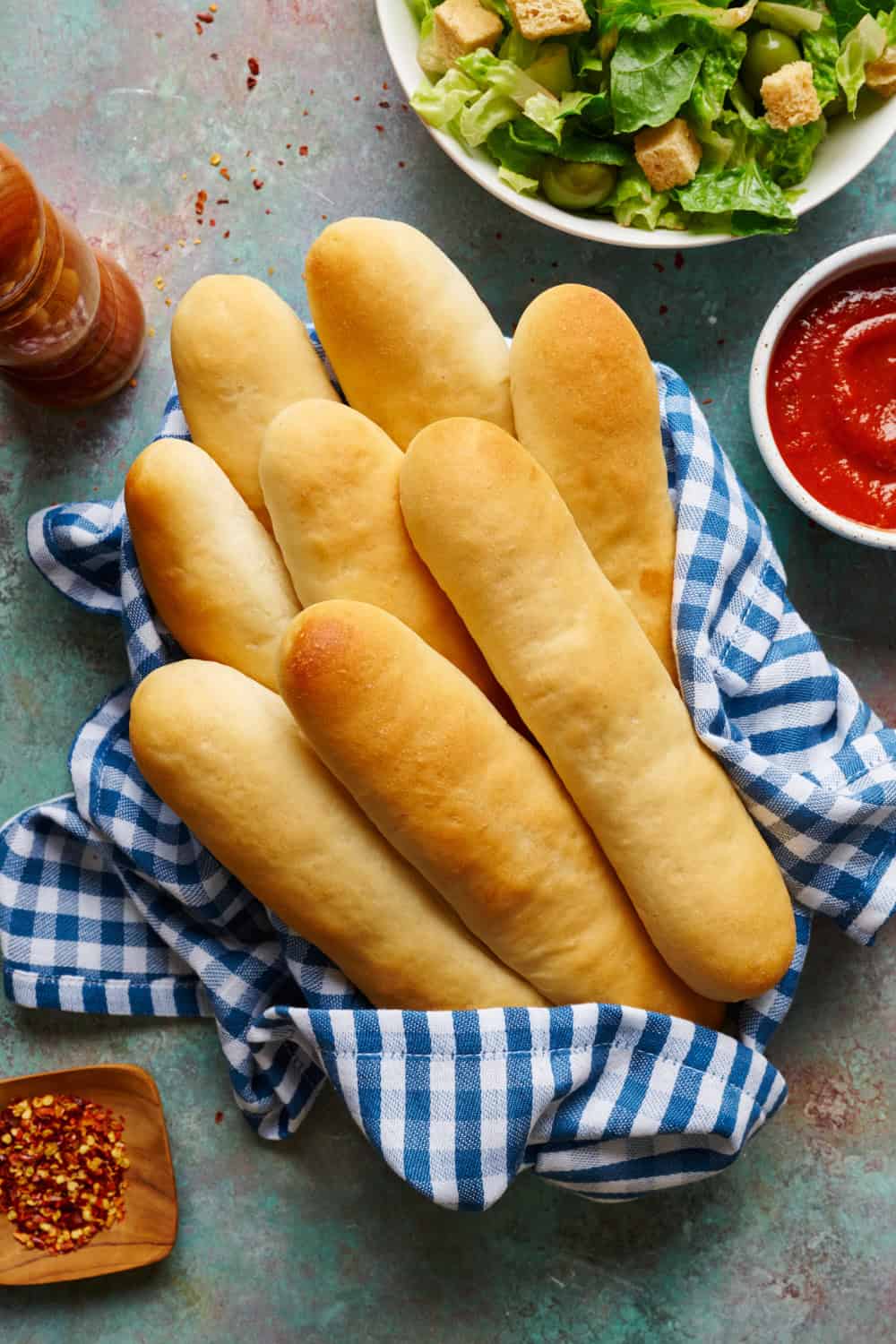 overhead view of soft sourdough breadsticks in a basket with gingham napkin