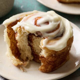 A cinnamon roll on a plate with a bite taken out and glossy frosting on top