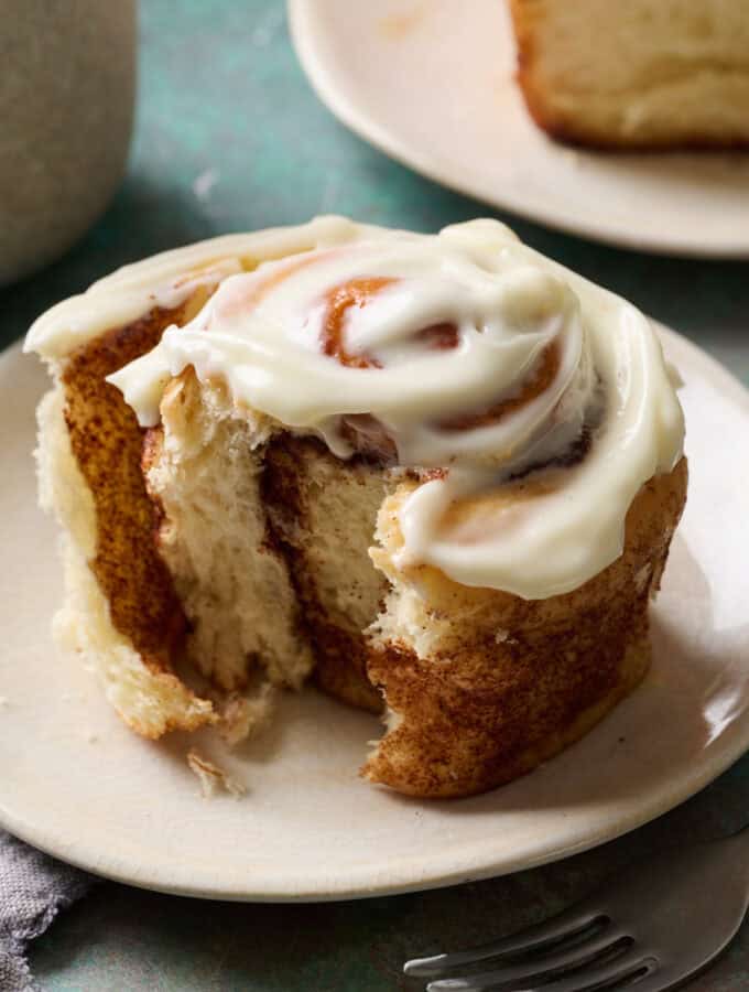 A cinnamon roll on a plate with a bite taken out and glossy frosting on top