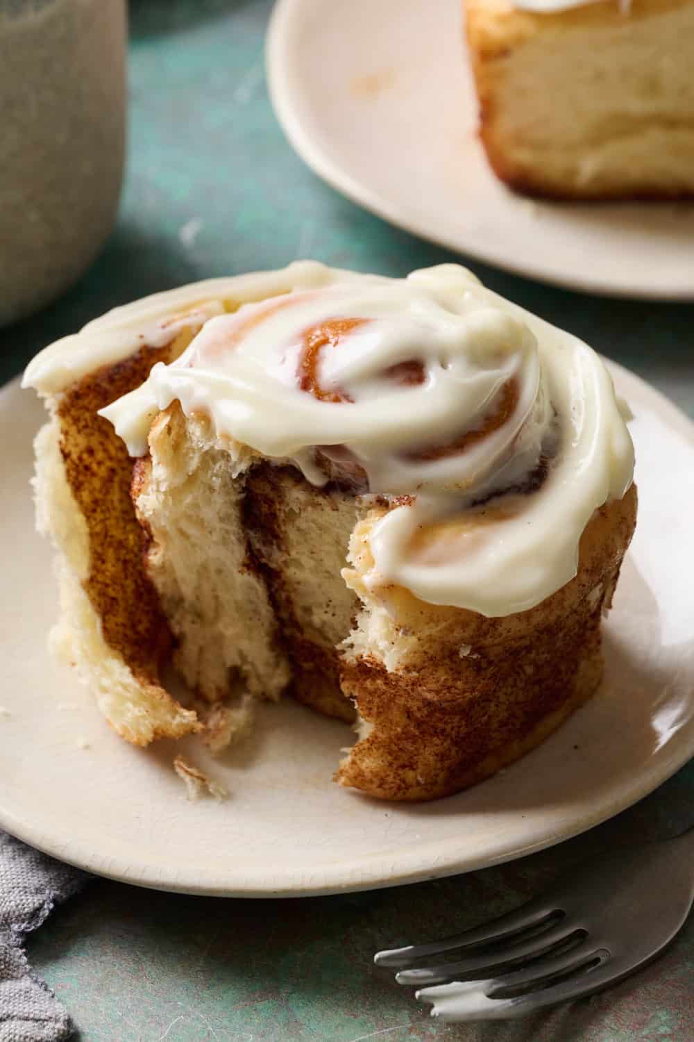 a cinnamon roll on a plate topped with frosting with a bite taken out