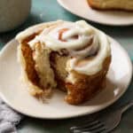 A sourdough discard cinnamon roll on a plate with a bite taken out