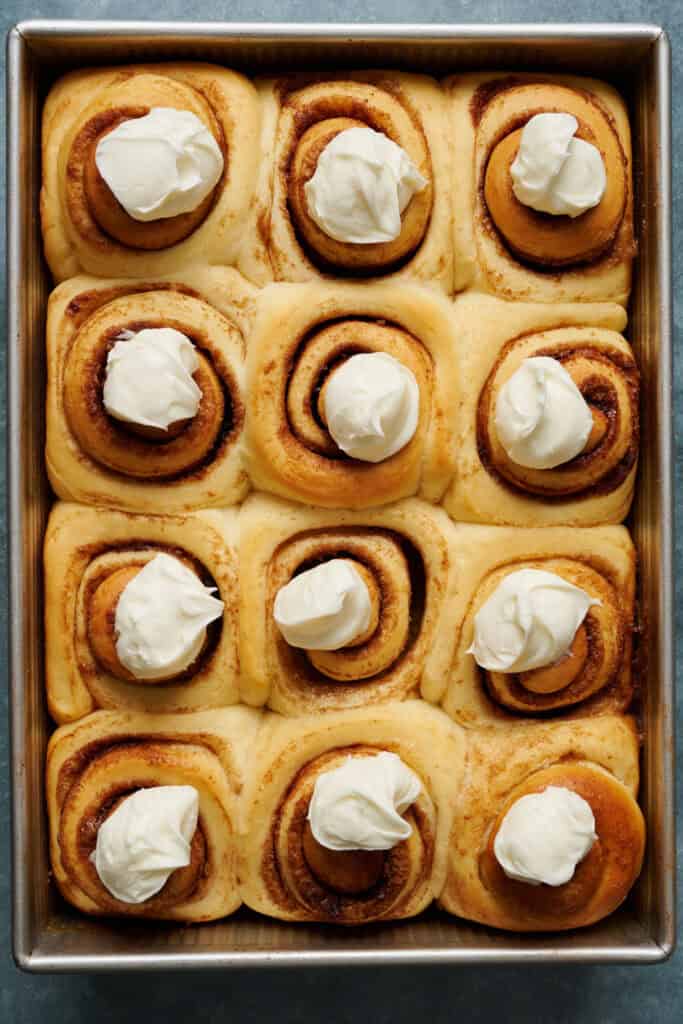 dollops of cream cheese frosting on cinnamon rolls ready to be spread