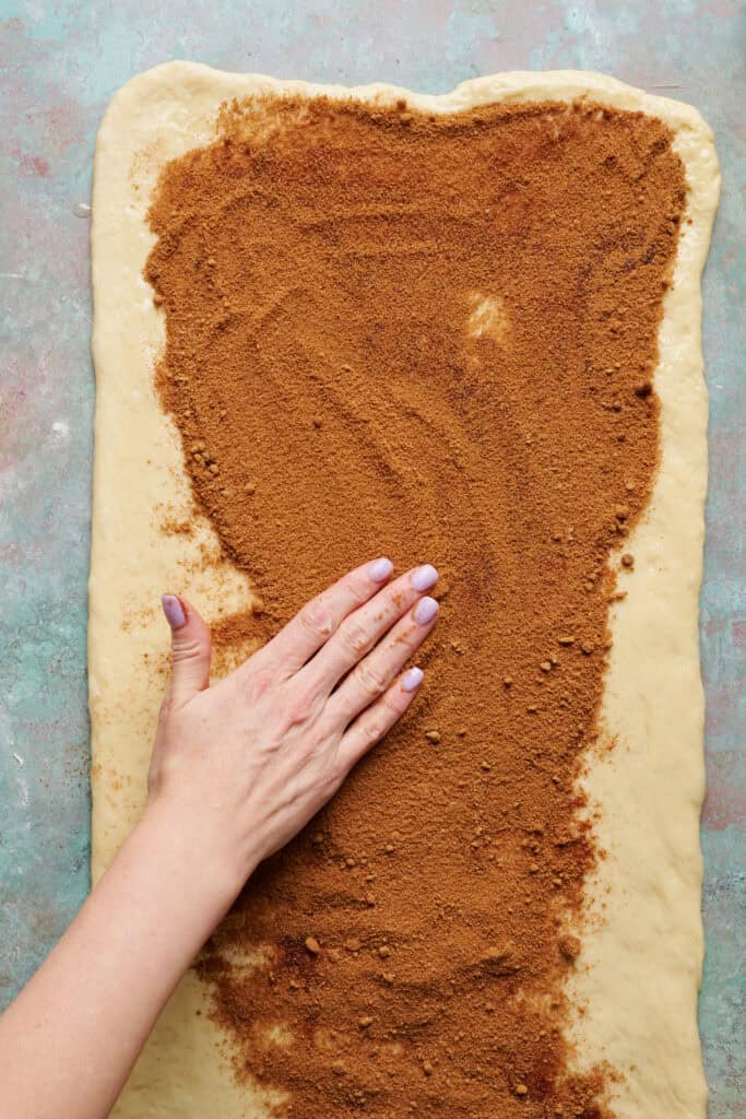 smoothing out cinnamon and sugar onto the rolled out dough