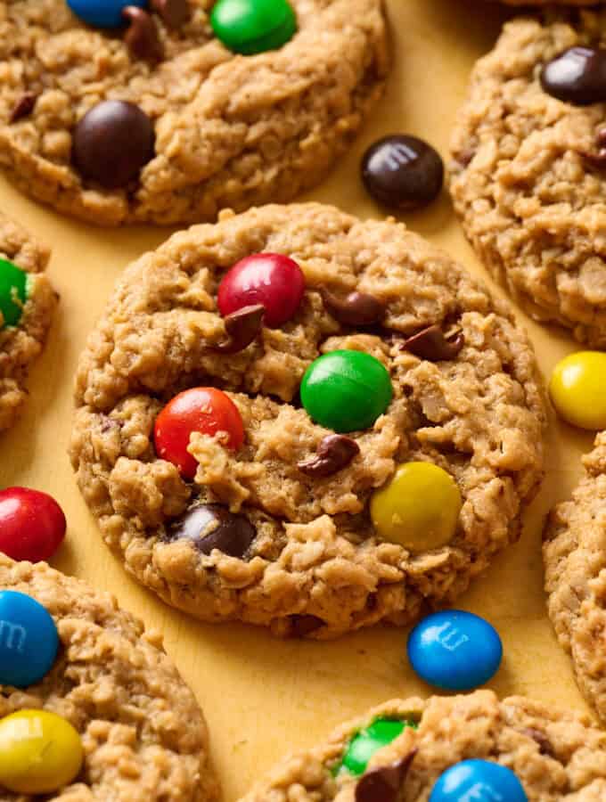 Side angle view of M&M, peanut butter, oatmeal cookies on a yellow background