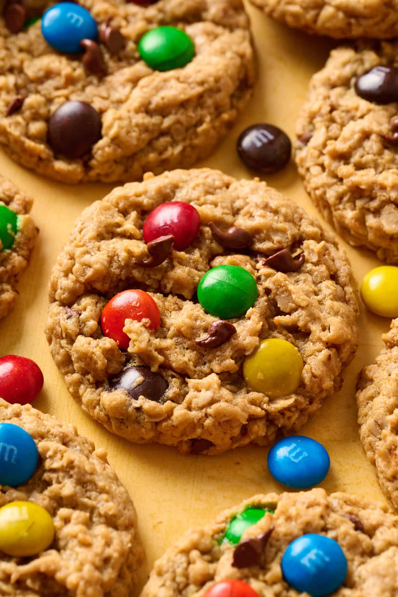 Side angle view of M&M, peanut butter, oatmeal cookies on a yellow background