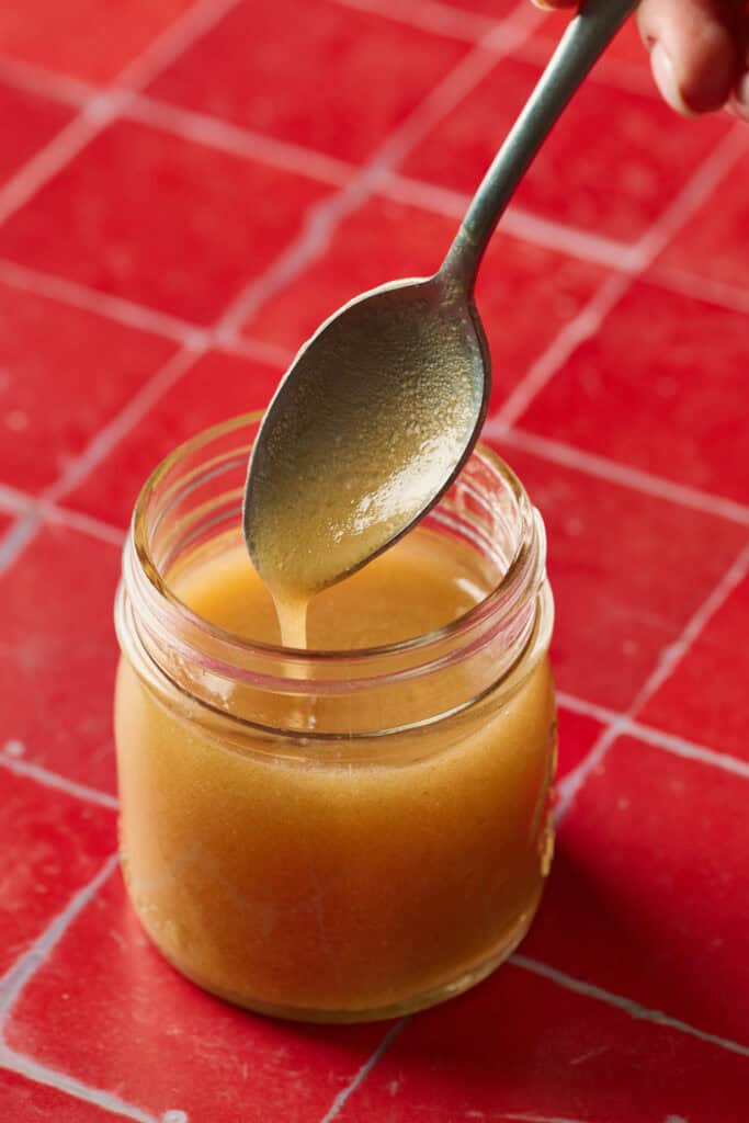 apple cider dressing in a jar with a spoon being lifted out