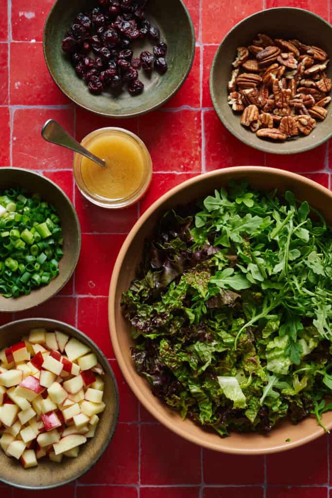 ingredients for salad including greens, apples, scallions, pecans and cranberries