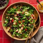 Arugula salad with apples, pecans, cranberries and scallions in a large salad bowl with tongs.