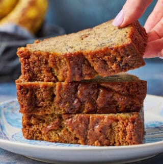 A stack of sourdough banana bread slices on a blue plate with a hand lifting the top slice