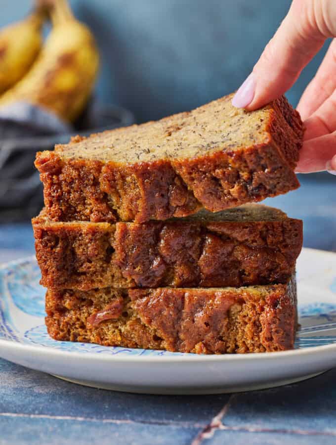 A stack of sourdough banana bread slices on a blue plate with a hand lifting the top slice