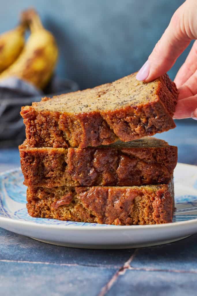 A stack of sourdough banana bread slices on a blue plate with a hand lifting the top slice