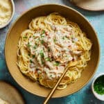 Creamy angel chicken pasta in a bowl with a fork topped with red pepper flakes and chives.