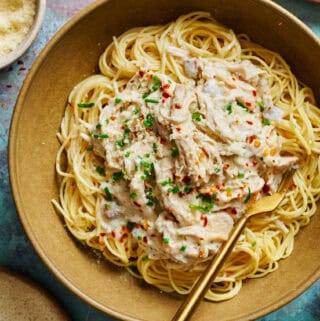 overhead view of a bowl of angel hair pasta topped with creamy chicken in a white sauce