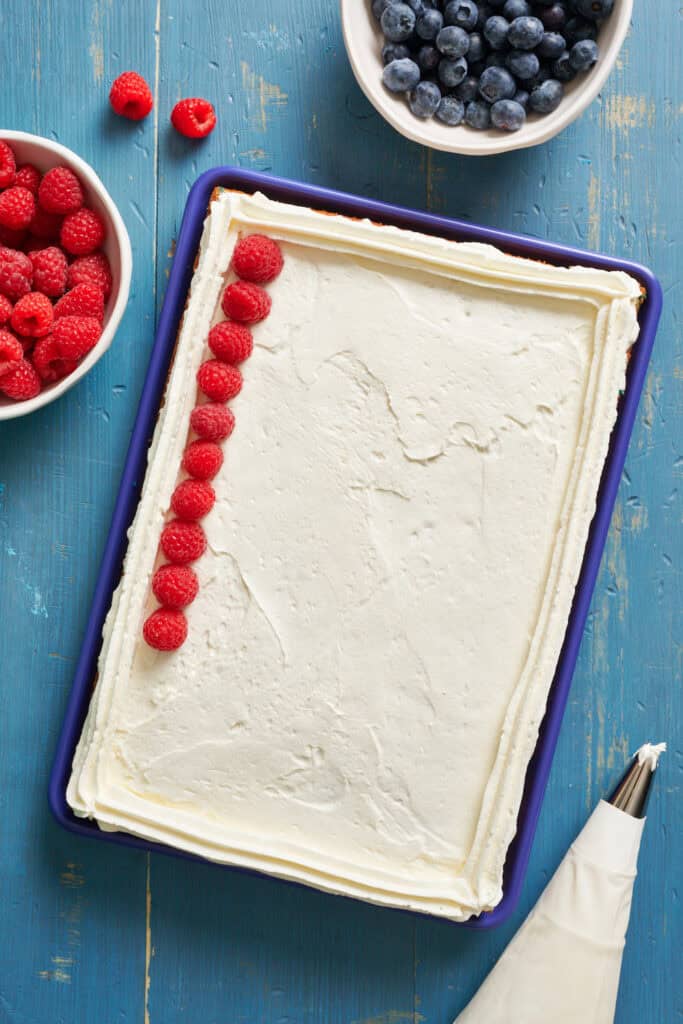 decorating a cake with white frosting and fresh raspberries and blueberries