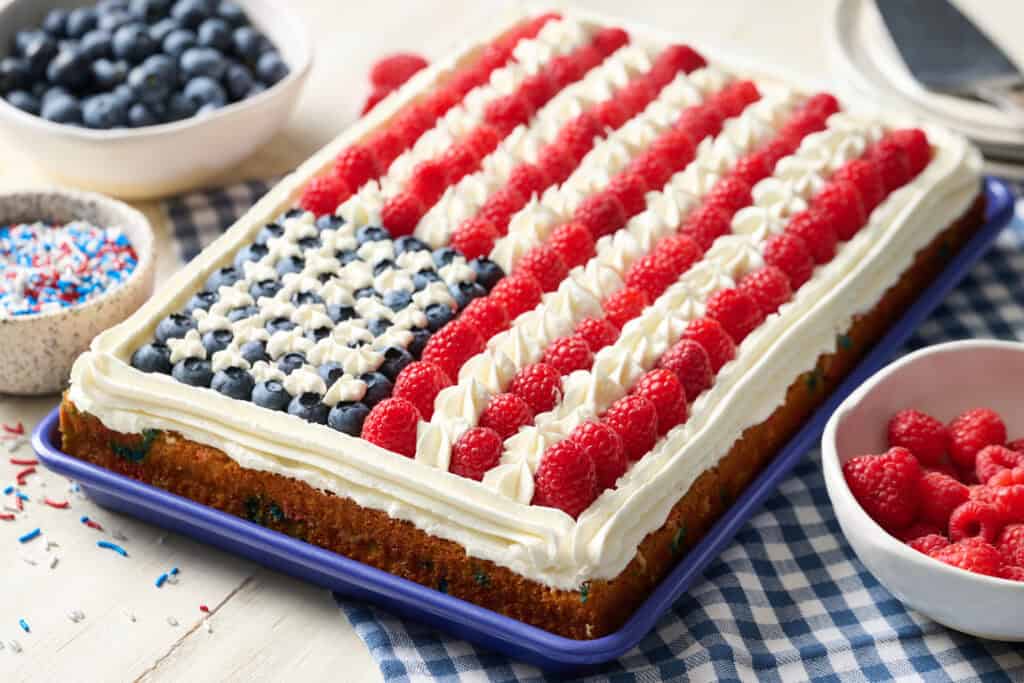 side view of a flag cake on a gingham napkin surrounded by more berries and serving plates for dessert