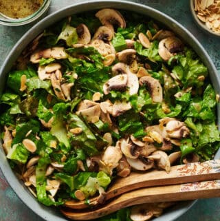 overhead view of a salad with mushrooms in a large bowl with salad tongs and dressing on the side