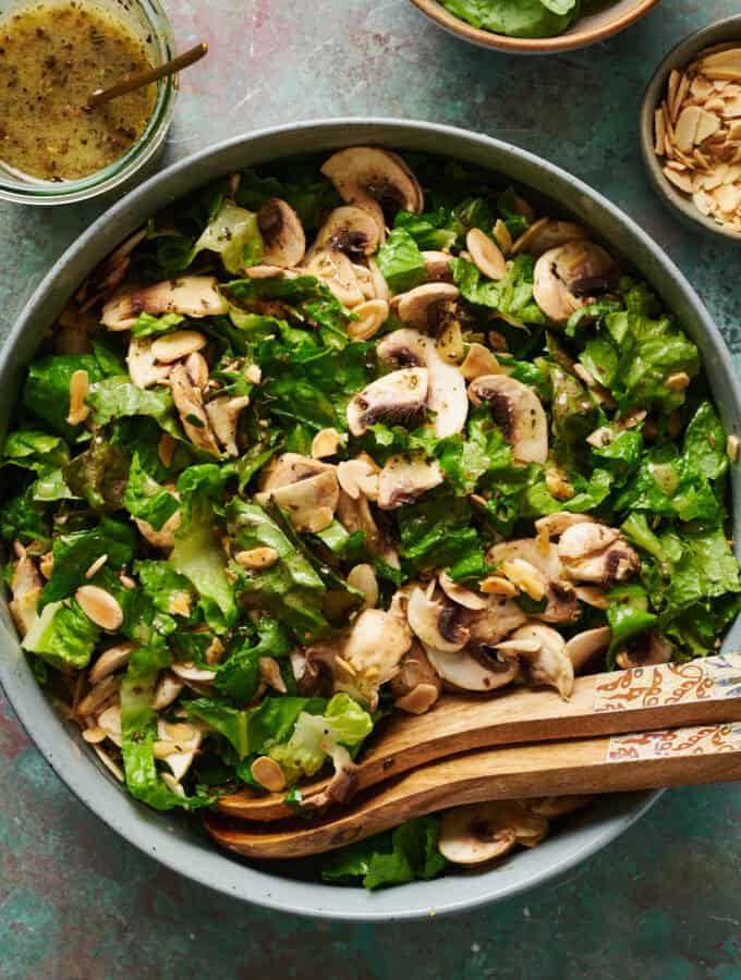 overhead view of a salad with mushrooms in a large bowl with salad tongs and dressing on the side