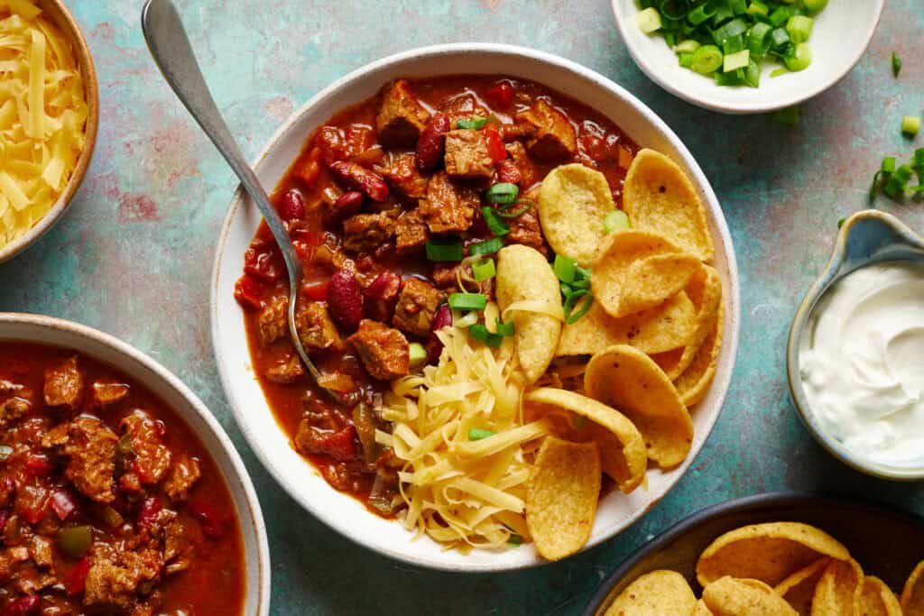 three bowls of chili filled with toppings, featuring beans and meaty steak