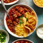 overhead view of a bowl of chili with corn ships, cheese and scallions.