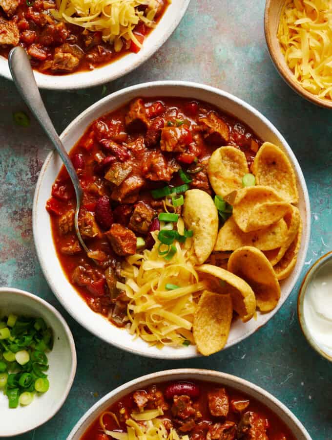 overhead view of three bowls of chili with chips, cheese and scallions