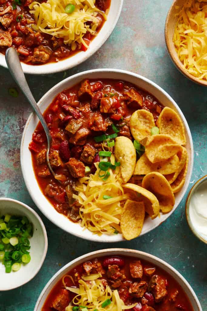 overhead view of three bowls of chili with chips, cheese and scallions