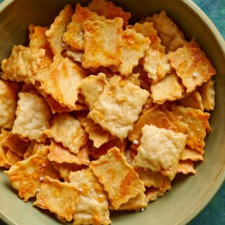 overhead view of a bowl of golden sourdough discard crackers on a green background