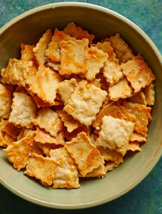 overhead view of a bowl of golden sourdough discard crackers on a green background