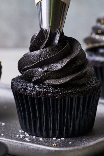 black velvet cupcakes on a plate surrounded by sprinkles, topped with black chocolate frosting