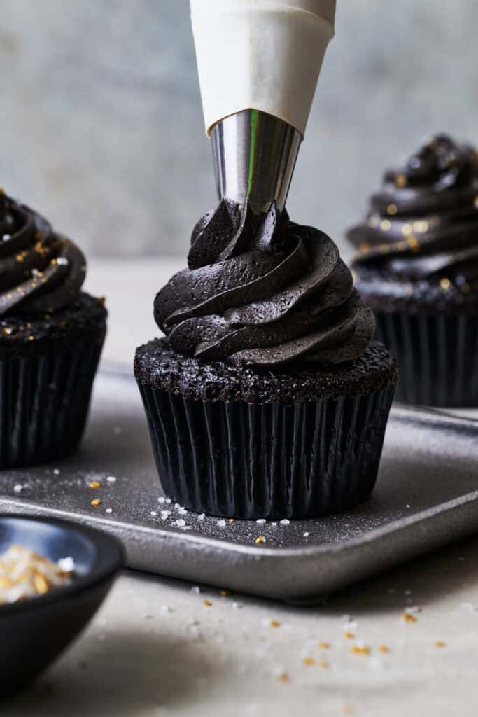 closeup piping black chocolate frosting onto black cupcakes