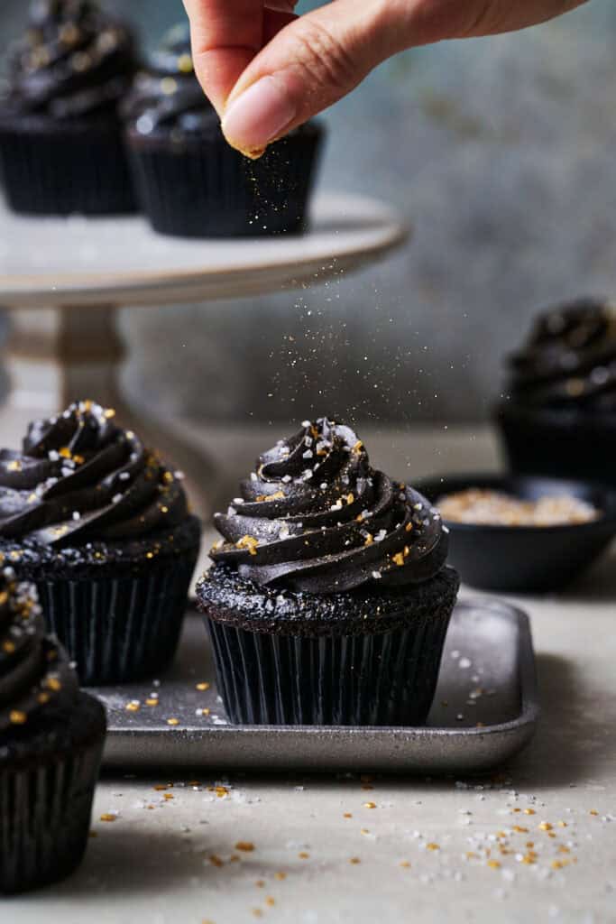 sprinkling sparkles on black velvet cupcakes