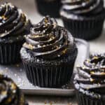 black velvet cupcakes on a plate surrounded by sprinkles, topped with black chocolate frosting