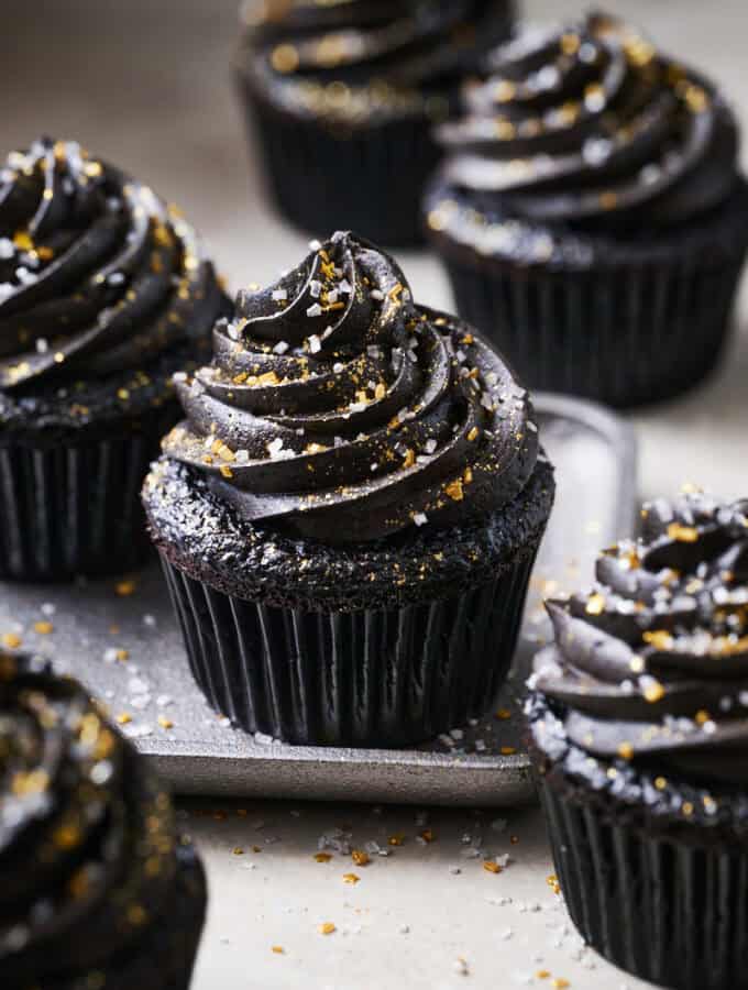 black velvet cupcakes on a plate surrounded by sprinkles, topped with black chocolate frosting