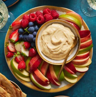 overhead view of a fruit platter with cheesecake fruit dip surrounded by apples, berries and grapes