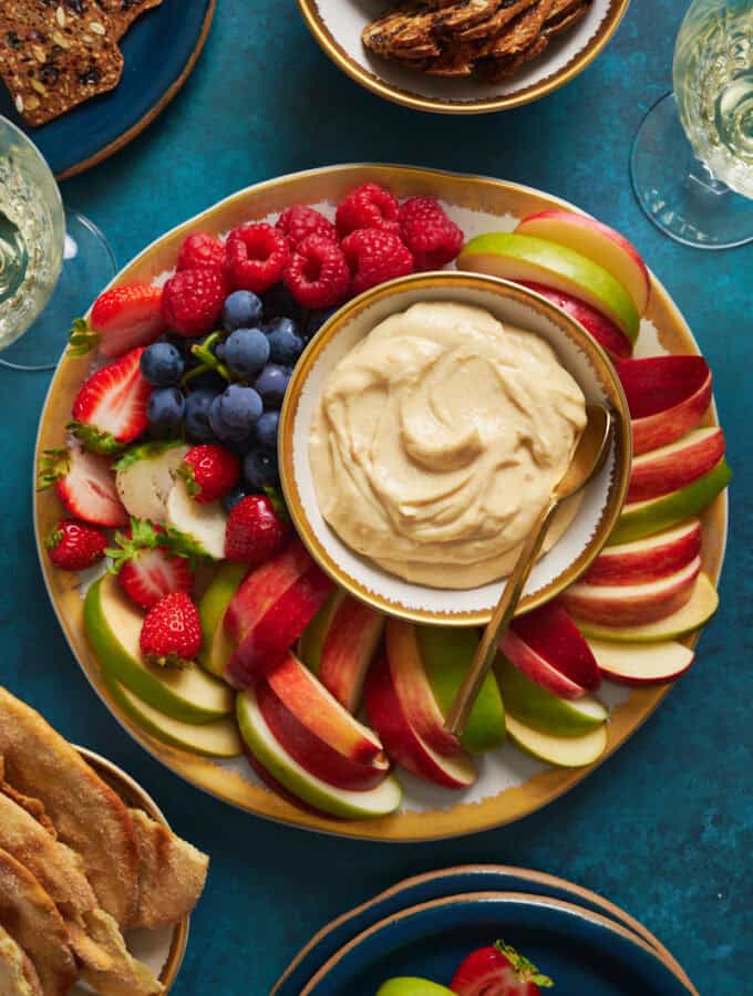 overhead view of a fruit platter with cheesecake fruit dip surrounded by apples, berries and grapes