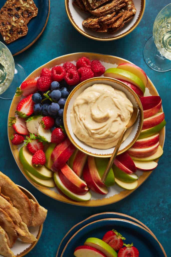 overhead view of a fruit platter with cheesecake fruit dip surrounded by apples, berries and grapes