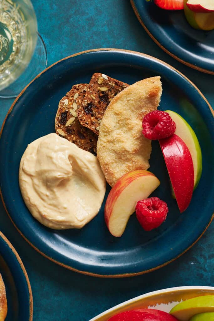 a single serving plate with a bit of cheesecake dip, a sweet cracker, berries and fruit