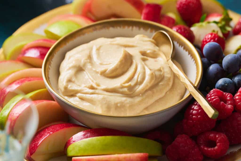 Cheesecake Fruit Dip in a bowl surrounded by fresh apples, berries and grapes.