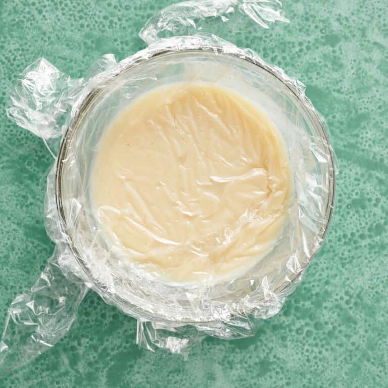 frosting base in a heat proof bowl with plastic on top