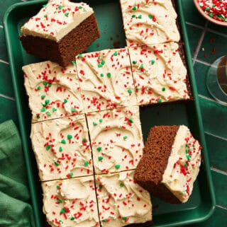 Gingerbread Cake with Cinnamon Molasses Frosting on a green sheet pan with a green napkin and tile background. Several slices removed from full cake.