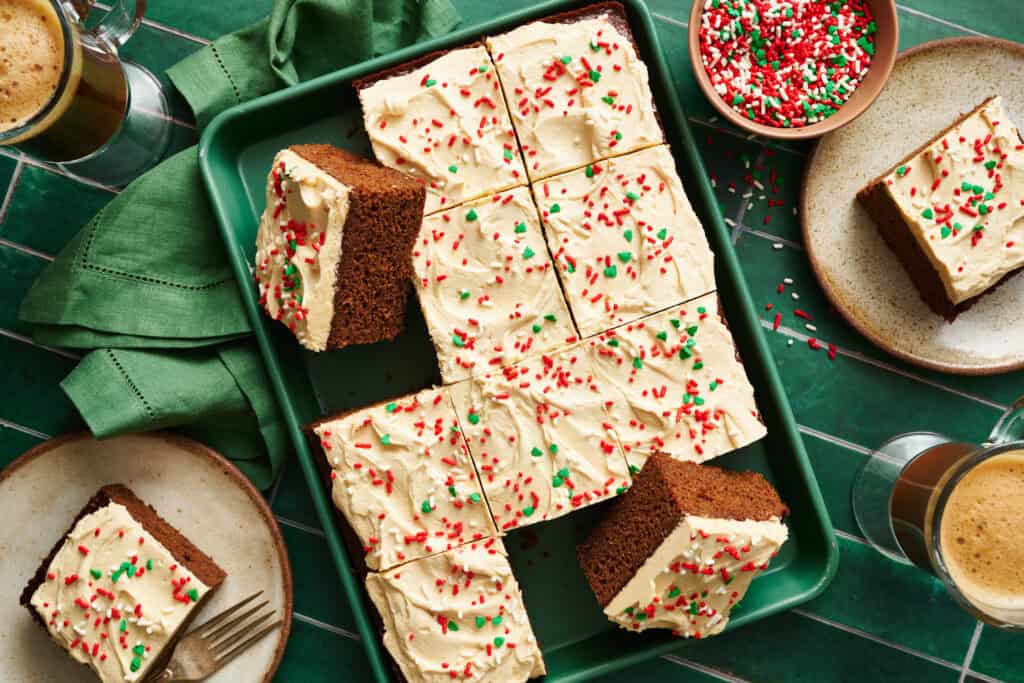 overhead view of a rectangular gingerbread cake with frosting on top and red and green sprinkles on a green background with a green napkin