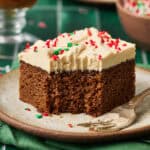 Slice of gingerbread cake with an ermine frosting in a scene with green tile and a fork has taken a bite out of the cake