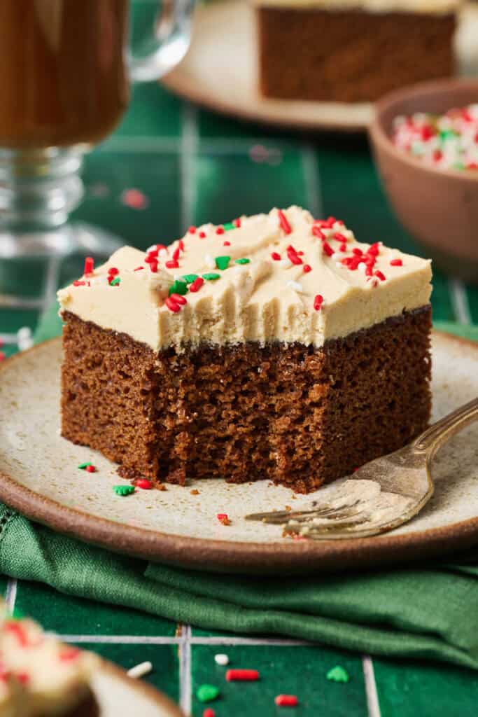 Gingerbread cake with ermine frosting on a plate with a bite taken out and a dirty fork on the plate