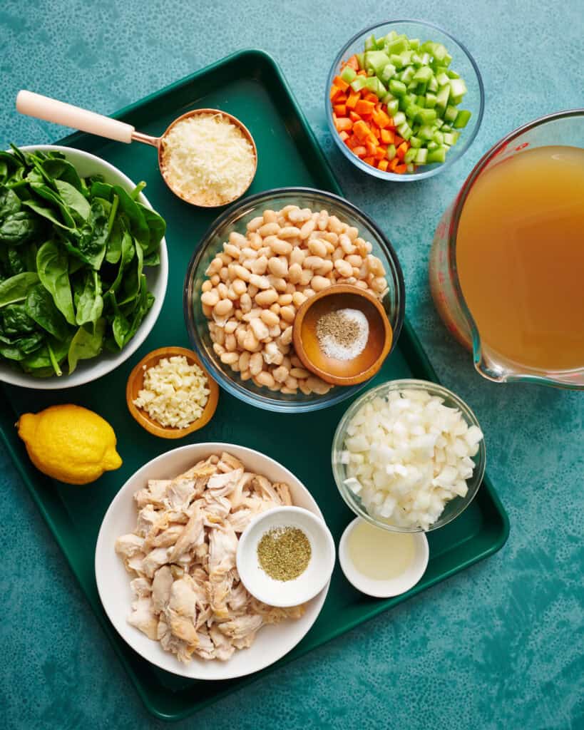 ingredients for this recipe all laid out including broth, onion, carrots, celery, garlic, parmesan cheese, shredded turkey or chicken, salt and pepper, lemon and spinach