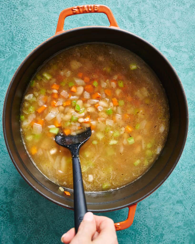 pot for soup filled with mirepoix, broth and white beans