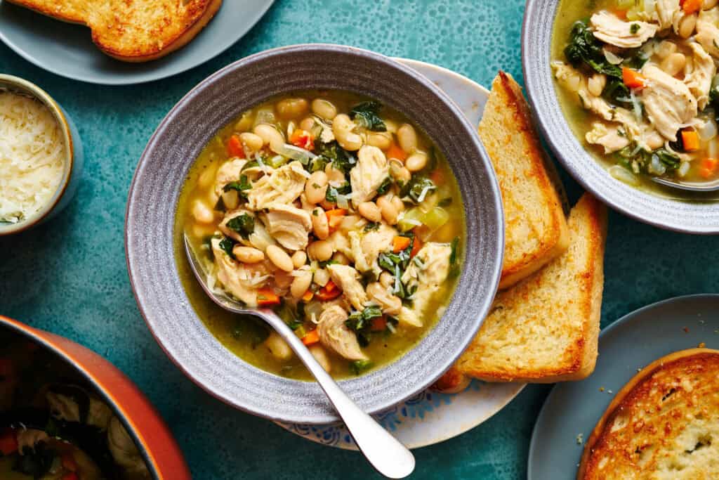 overhead view of a bowl of lemon white bean soup with turkey and greens with toasted bread on the side