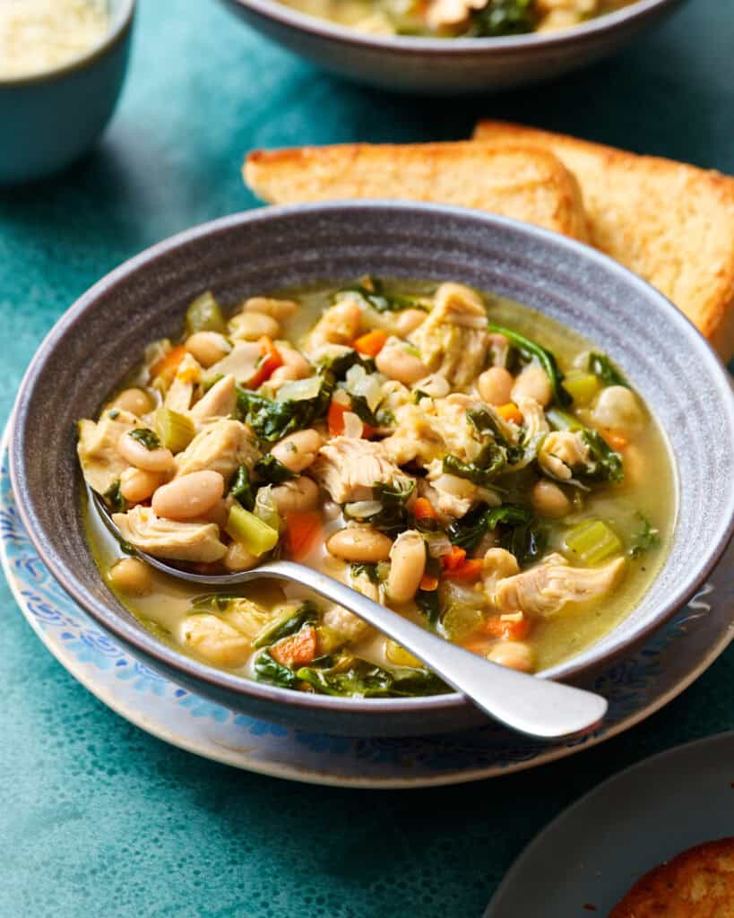 Side view of a bowl of soup with shredded turkey, vegetables and a broth with greens and white beans