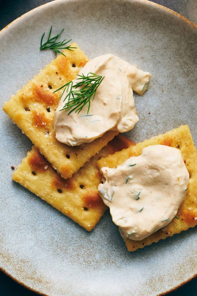 Crackers with spicy dill pickle dip smeared on and fresh dill on top